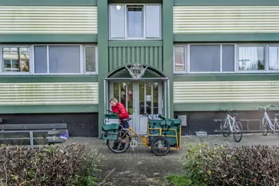 Kvinde med sin postcykel foran en opgang i boligafdelingen Stengårdsvej.