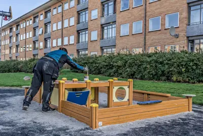 Kvindelig medarbejder maler træværk på legeplads foran lejlighedskompleks i Sundparken